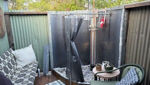 Un petit espace extérieur comprenant une douche en métal, une chaise verte, un canapé à motifs et une petite table agrémentée de plantes en pot.