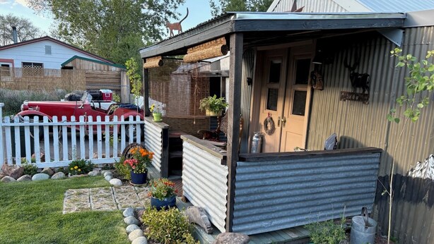 Un petit bâtiment d’un seul étage, avec une façade en métal ondulé, une terrasse en bois et une clôture blanche faite de piquets.
