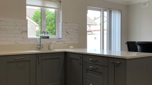 A modern kitchen with grey cabinets, a white countertop, a window with a view, and a black chair. - Galway City Stayin quant neighbourhood (Galway)