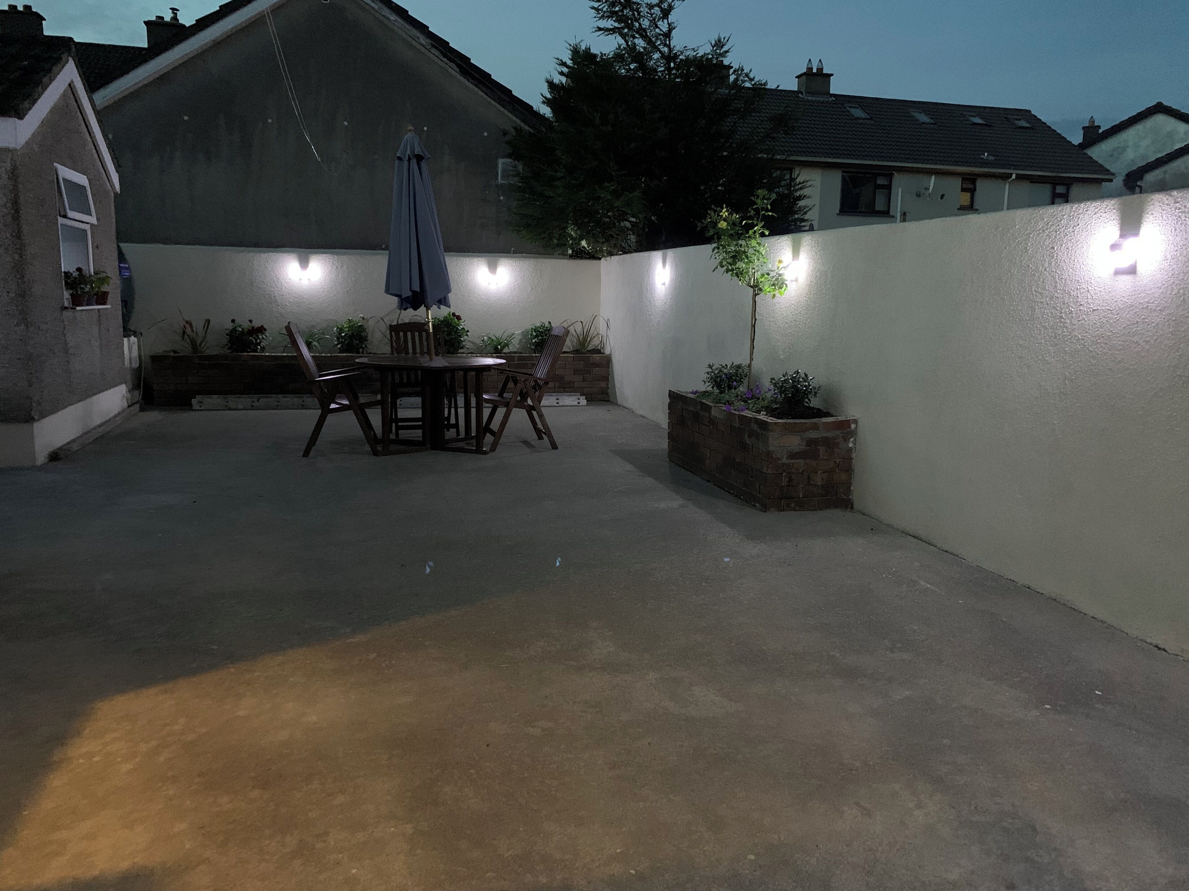 Une terrasse avec une table et des chaises, un pot de fleurs et un mur décoré de guirlandes lumineuses.
