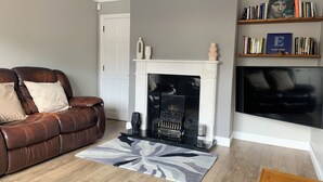 A living room with a leather sofa, a fireplace, a bookshelf, and a flat-screen TV. - Galway City Stayin quant neighbourhood (Galway)