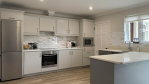 A modern kitchen with white cabinetry, a marble backsplash, a stainless steel refrigerator, an oven, a microwave, and a large island. - Galway City Stayin quant neighbourhood (Galway)
