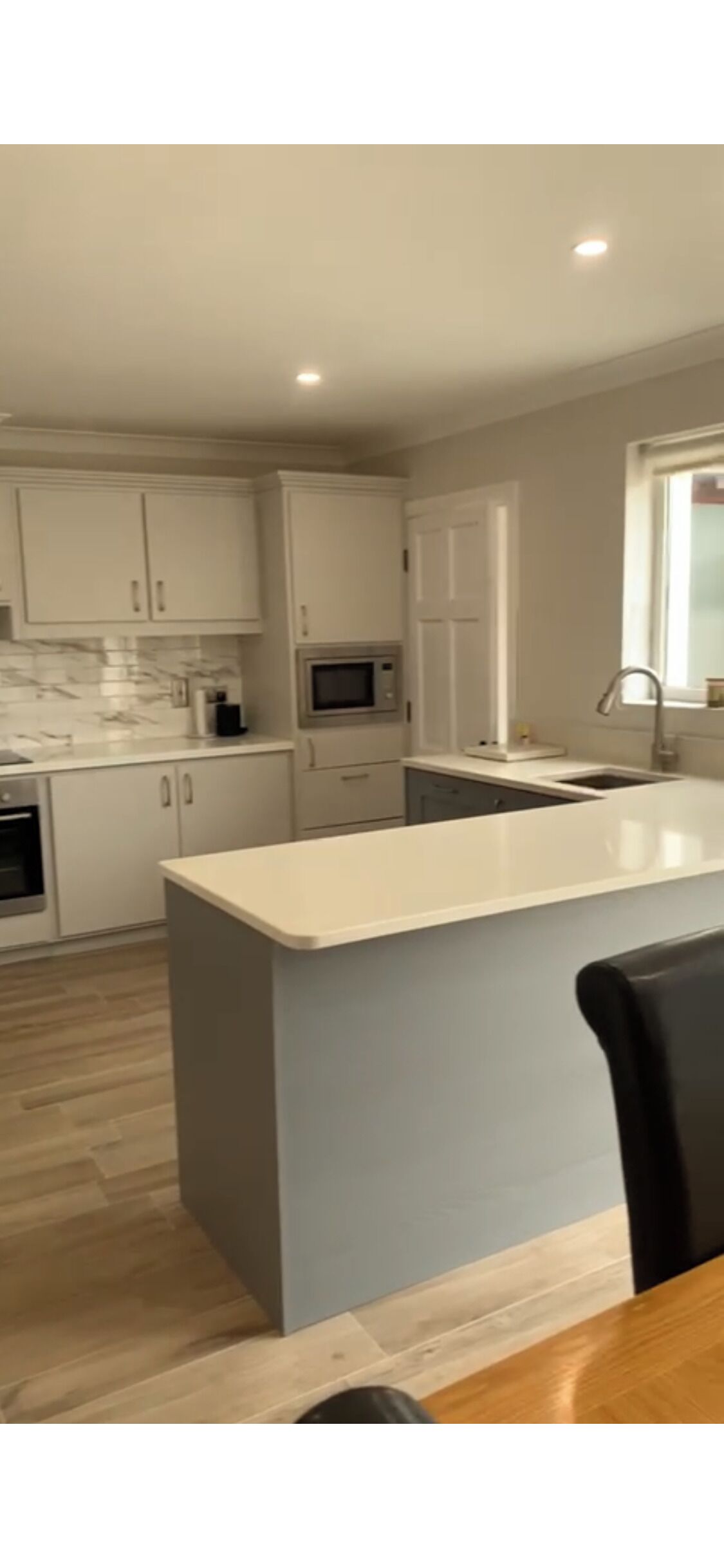 A modern kitchen with white cabinets, a marble backsplash, a central island, and a built-in microwave.