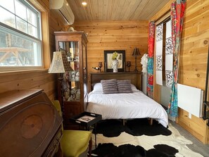 A wooden cabin bedroom with a bed, a dresser, a lamp, and a window.
