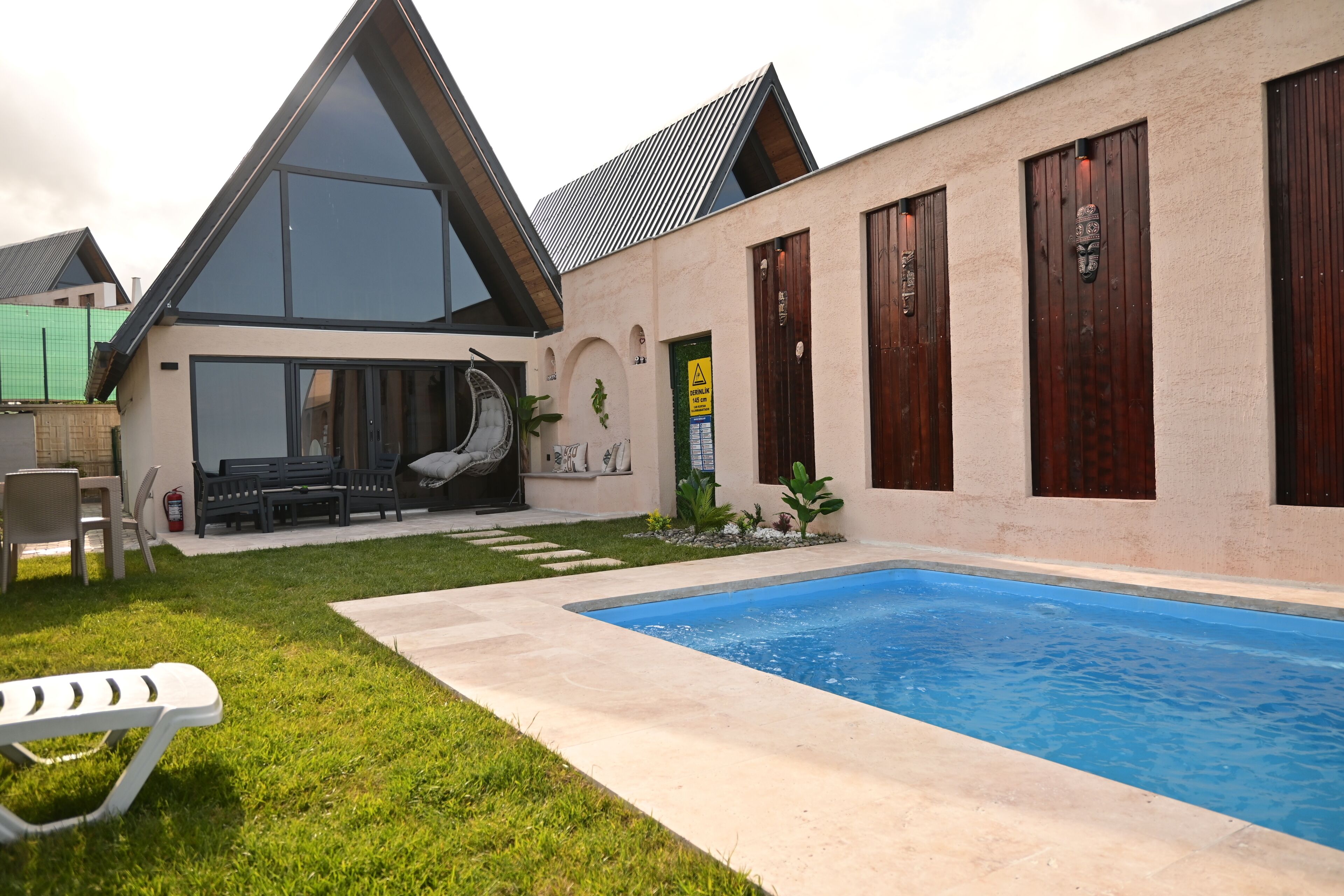 Una casa moderna con piscina, un patio con mobiliario exterior y un ventanal grande.