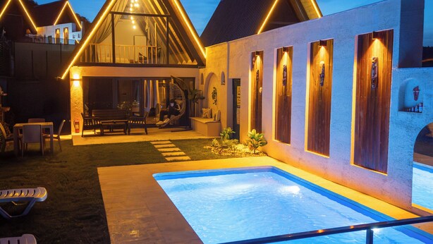 A modern building with a swimming pool, outdoor seating, and a well-lit entrance.