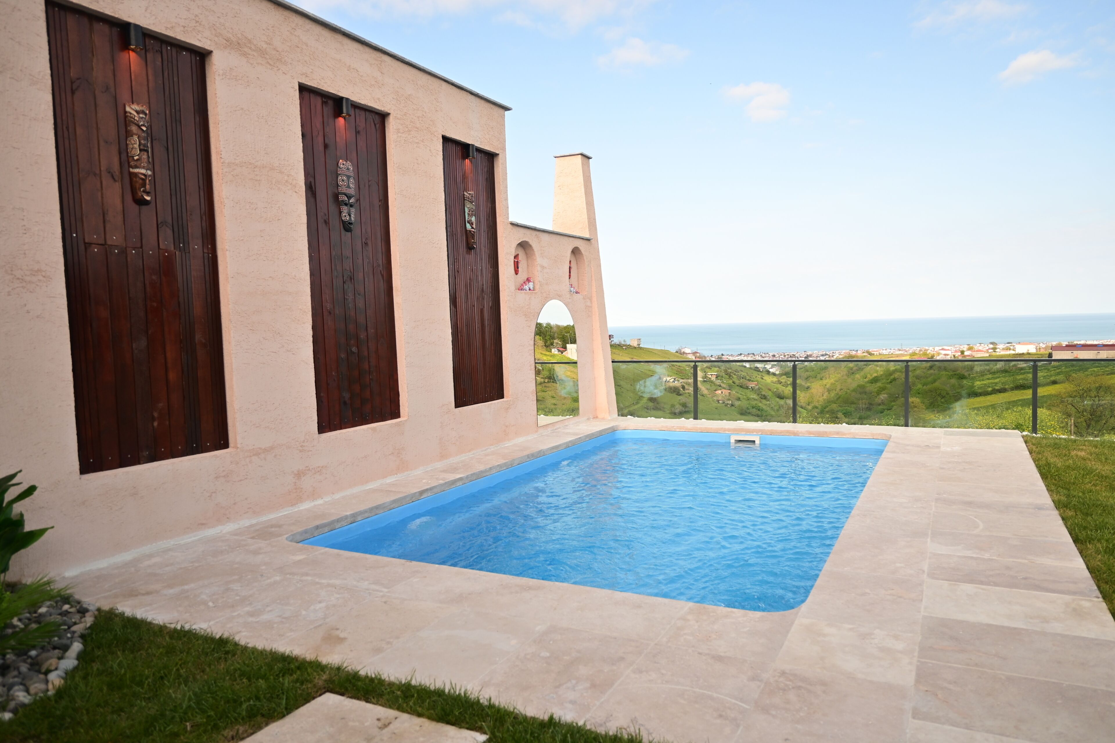 Ein Pool mit Meerblick, ein Gebäude mit Holztüren und eine Rasenfläche.