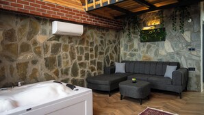 A room with a stone wall, a white bathtub, a gray sofa, and a wooden ceiling.