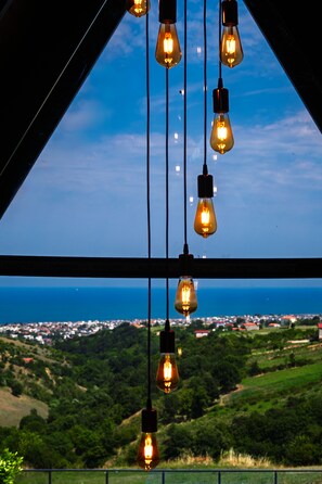 Vista a través de una ventana con bombillas colgantes, cielo despejado y un paisaje distante.
