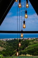 Vista a través de una ventana con bombillas colgantes, cielo despejado y un paisaje distante.