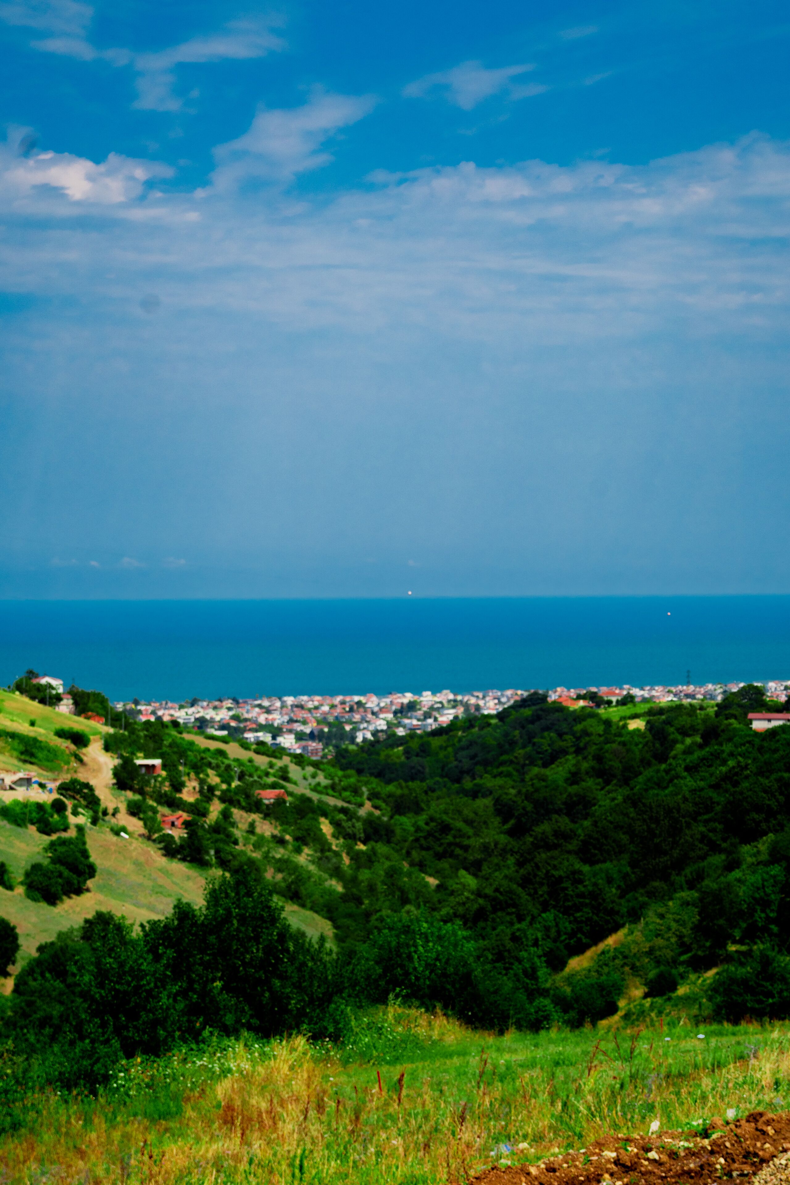 Un paisaje costero con un pueblo en el valle, colinas verdes y el mar.
