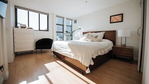 Una camera da letto con un letto, un comodino, una lampada, una cassettiera e delle finestre.