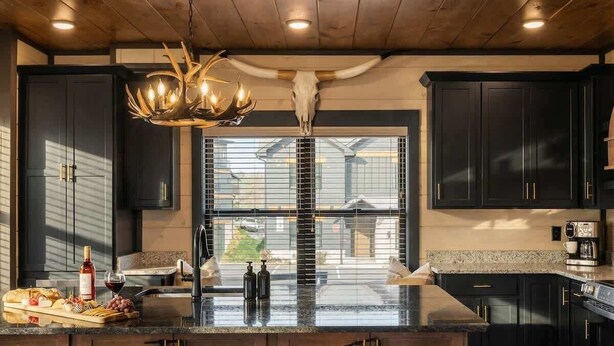 A modern kitchen with dark cabinetry, a central island with stools, a chandelier, and a large window. - Cabin near Dollywood w/ pool & hot tub (Sevierville)