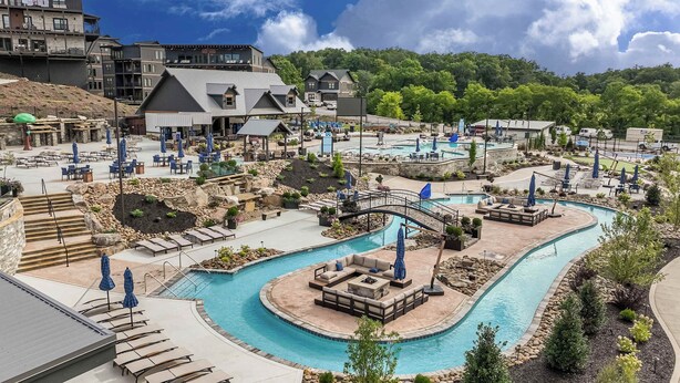 Et resort med en stor swimmingpool, udendørs siddepladser og et bjerglandskab i baggrunden.