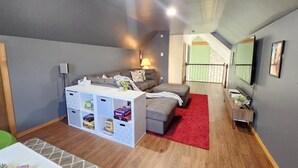 A modern living room with a grey sofa, a white entertainment unit, a red rug, and a small table with a lamp. - Arrowhead Community Hot Tub Firepit Game Rm Movie Rm Fireplace Walk 2 Pool, Lake (Pocono Lake)