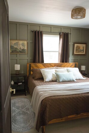 A bedroom with a wooden bed, a nightstand, a lamp, a rug, and a painting on the wall.