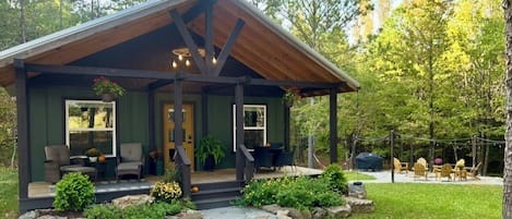 A cabin with a porch, outdoor seating, and a grill area.
