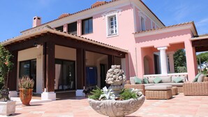 A pink villa with a covered patio, outdoor seating, and a large planter with plants. - 10-PERSON VILLA WITH LARGE POOL NEAR ROCK AND LAKE (Roquebrune-sur-Argens)