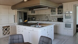 A modern kitchen with white cabinetry, a central island with a sink, and built-in appliances including a microwave and oven. - 10-PERSON VILLA WITH LARGE POOL NEAR ROCK AND LAKE (Roquebrune-sur-Argens)