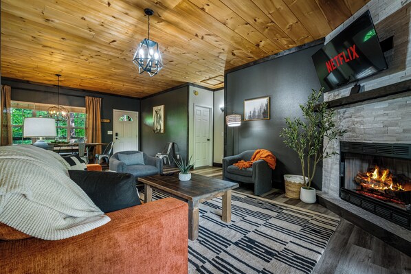 A living room with a fireplace, a mounted TV, and a wooden ceiling. - New Listing! Hot Tub, Arcade, Close 2 Parkway! (Pigeon Forge)