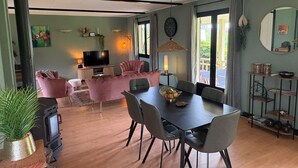 A modern living room with a TV, pink sofas, a dining table with chairs, and a large window.