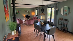 A modern living room with a TV, pink sofas, a dining table with chairs, and a large window.