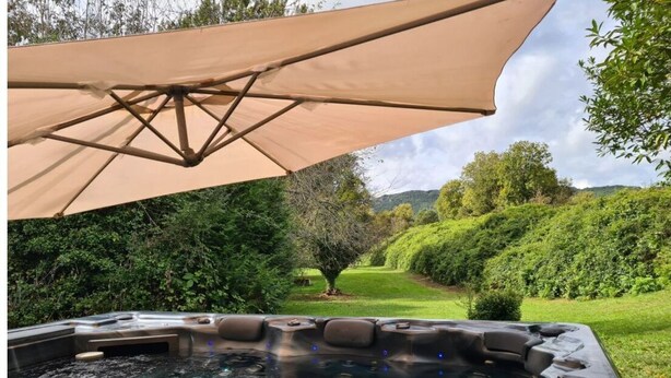 A hot tub with a canopy, surrounded by lush greenery and hills.