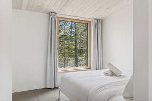 A bedroom with a large window, a bed, and a rolled towel on the bed. - The Lost Lake Residence (Wentworth-Nord)