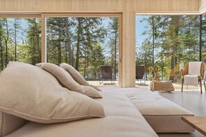 A modern room with a large bed, a sofa, and a chair, all facing large windows with a forest view. - The Lost Lake Residence (Wentworth-Nord)