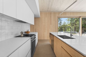 A modern kitchen with white cabinets, a wooden countertop, a sink, and a view of the outdoors. - The Lost Lake Residence (Wentworth-Nord)
