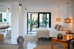 Un dormitorio moderno con cama, mesitas de noche, un espejo y vistas a un balcón con plantas a través de un ventanal.