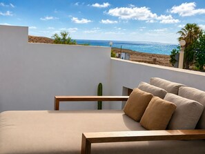 Un balcón con una cama, un cactus y vista al mar.