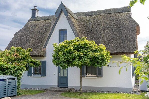Une maison traditionnelle avec un toit de chaume très pentu, une petite porte d’entrée et une fenêtre avec des volets.