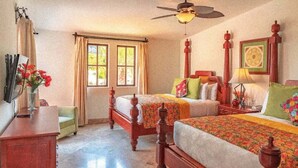 Ein Hotelzimmer mit zwei Holzbetten, einem Deckenventilator, einem Schreibtisch, einem Stuhl und einem Fenster mit Vorhängen.