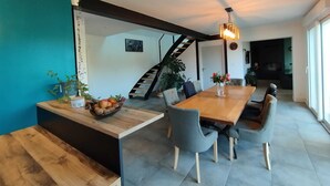 Een moderne eetruimte met een houten tafel, grijze stoelen en een trap naar een hoger niveau.