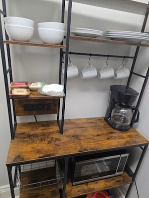 Een keuken met een koffiezetapparaat, een magnetron en planken met kommen en kopjes.
