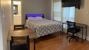 Un dormitorio con cama, escritorio, silla, ventilador de techo y televisor.