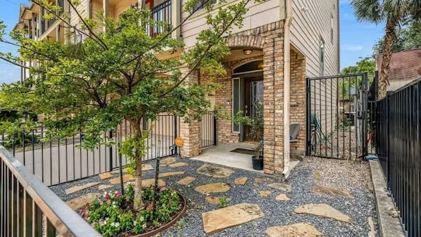 Un edificio de varios pisos con fachada de piedra, entrada porticada y un pequeño jardín con un árbol y flores.