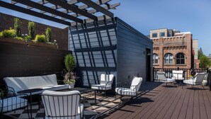 Eine Terrasse im Freien mit einer Pergola, einer Sitzgelegenheit und Blick auf ein Backsteingebäude.
