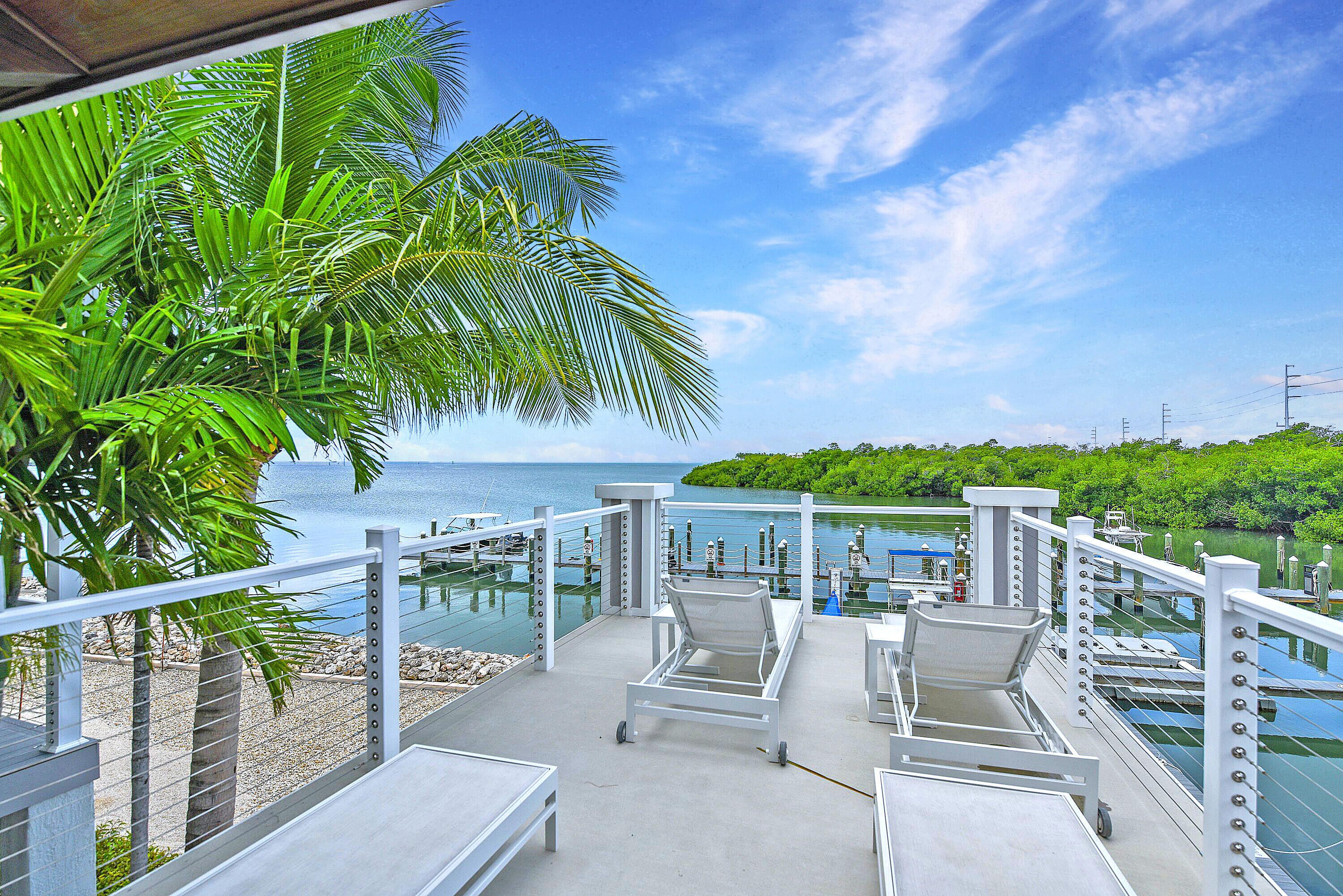A balcony with lounge chairs overlooking a marina and the sea.