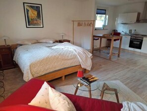 Een slaapkamer met een bed, nachtkastje, lamp en een klein tafeltje met een boek en lekkernijen.