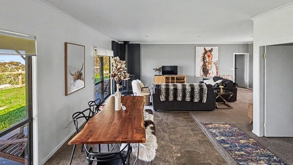 A modern living room with a dining area, a sofa, a TV, and artwork on the walls.