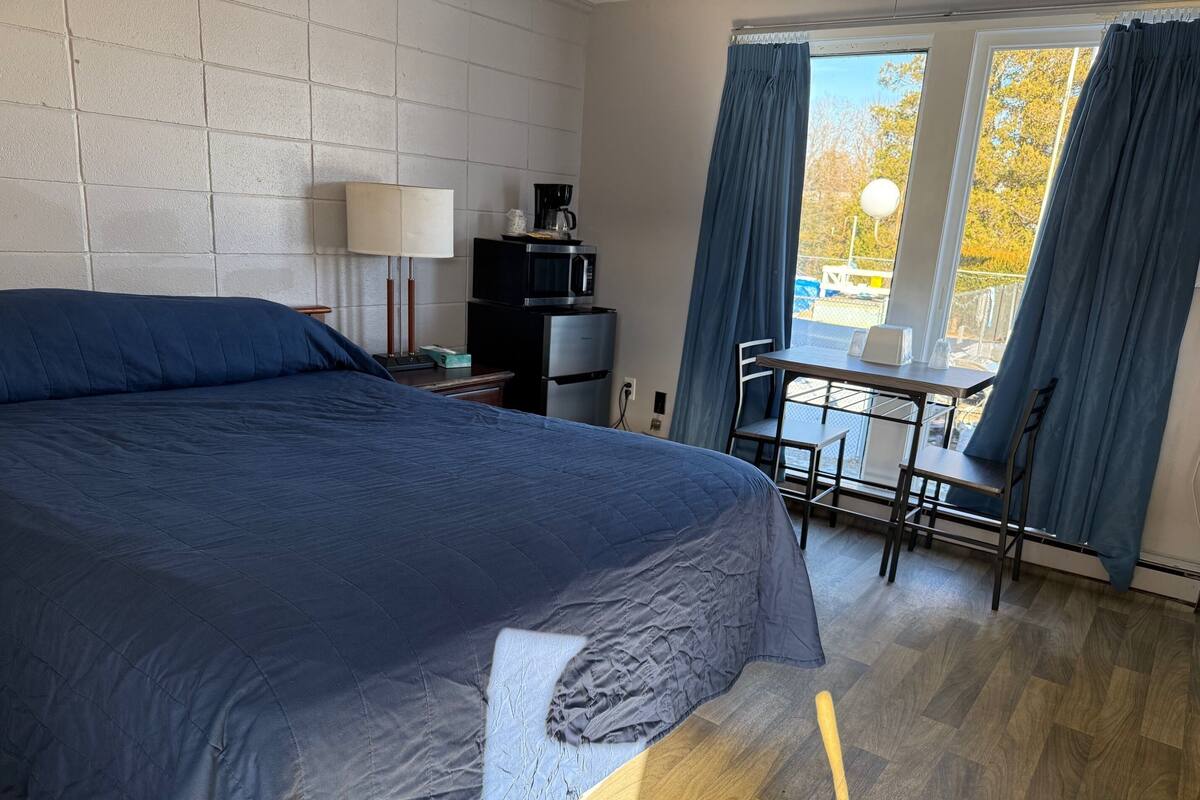 A bedroom with a large bed, a desk, a chair, a lamp, and a window with curtains.