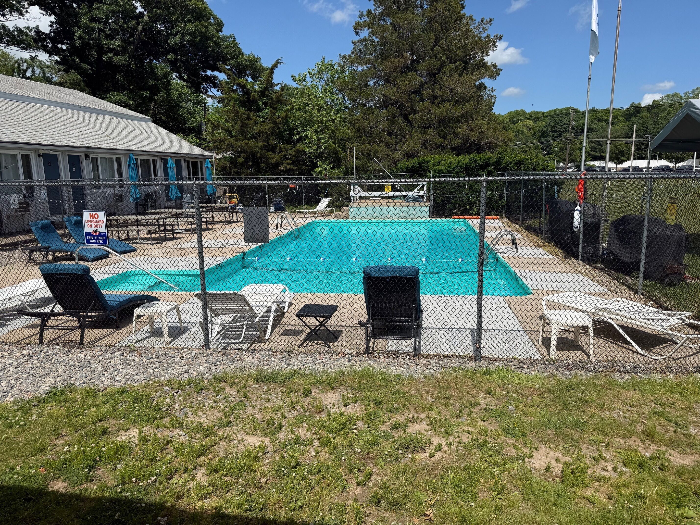 A fenced outdoor swimming pool with lounge chairs and a no lifeguard on duty sign.