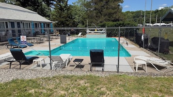 A fenced outdoor swimming pool with lounge chairs and a no lifeguard on duty sign.