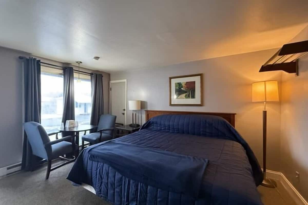 A hotel room with a bed, a desk, a chair, a lamp, and a window with curtains.