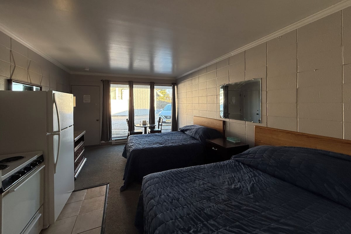 A hotel room with two beds, a kitchenette, a TV, and a sliding glass door to the outside.