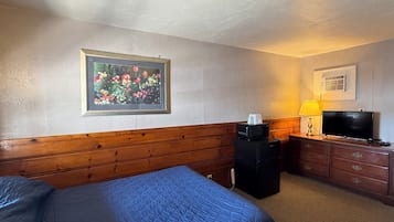 Habitación de hotel con una cama, televisión, microondas, lámpara y un cuadro en la pared.
