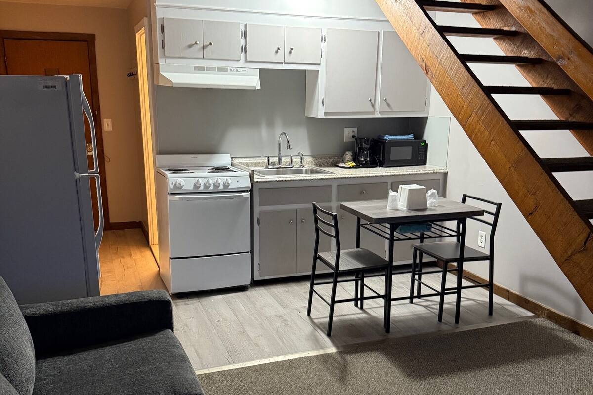 A compact kitchen with white cabinets, a stove, and a dining area with a table and chairs.