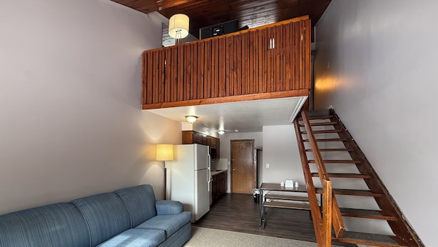 Espaço de estar estilo loft com sofá azul, escada de madeira e cozinha.